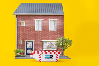 Huisgevel (model) staat rechts in beeld, met voordeur, planten en een rood-wit bouwhek ervoor; felle gele achtergrond vult de rest van het minimalistische tafereel.
